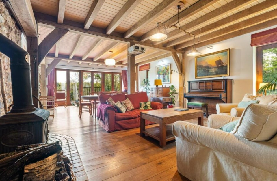 Interior view of a large living room with exposed wooden beams, a wood-burning stove, and comfortable sofas.