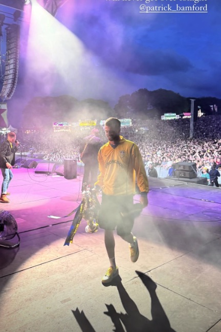 Man in yellow shirt carrying trophy on stage in front of a large crowd.