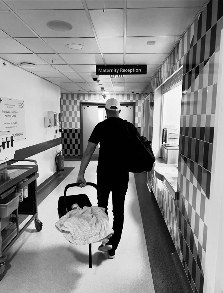 Man carrying baby in car seat down hospital hallway.