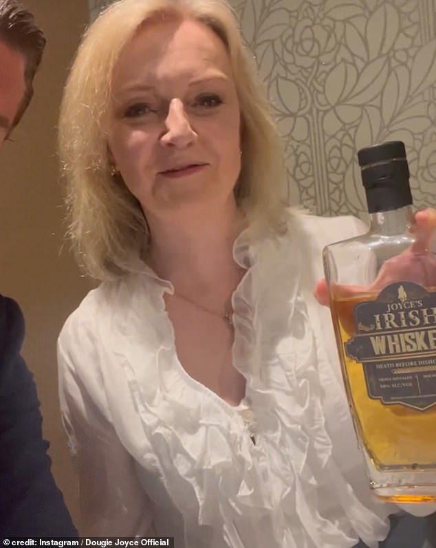 After Joyce points to the lens and says, 'just remember Dougie Joyce loves ya', Ms Truss, who led the nation for 49 days in 2022, repeats his catchphrase while holding a bottle of the booze