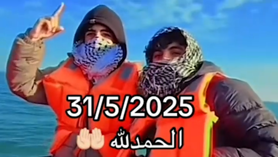 Two migrants wearing life vests and face coverings on a boat.