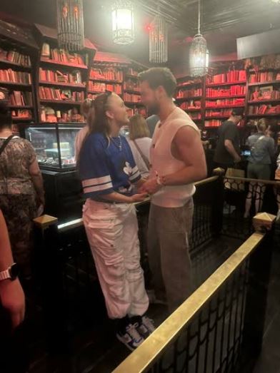 Couple standing in a library, holding hands.