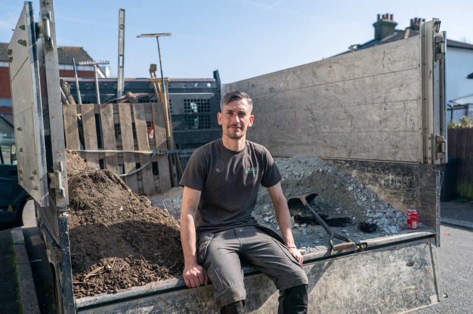 Landscaper sitting in the back of a truck filled with soil and gravel.