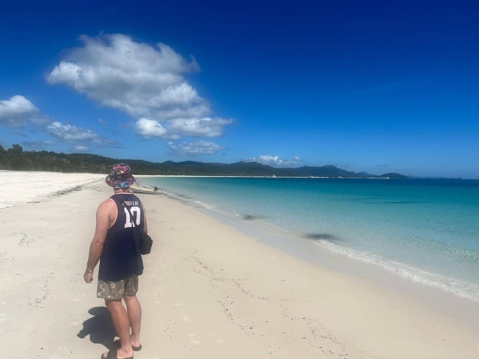 Man walking on a white sand beach towards turquoise water.