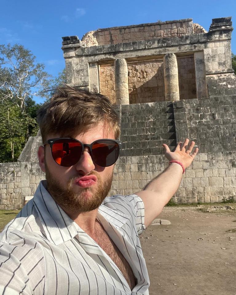 Man in sunglasses gesturing towards Mayan ruins.