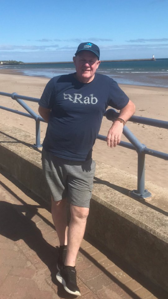 Man standing by a railing on a beach.
