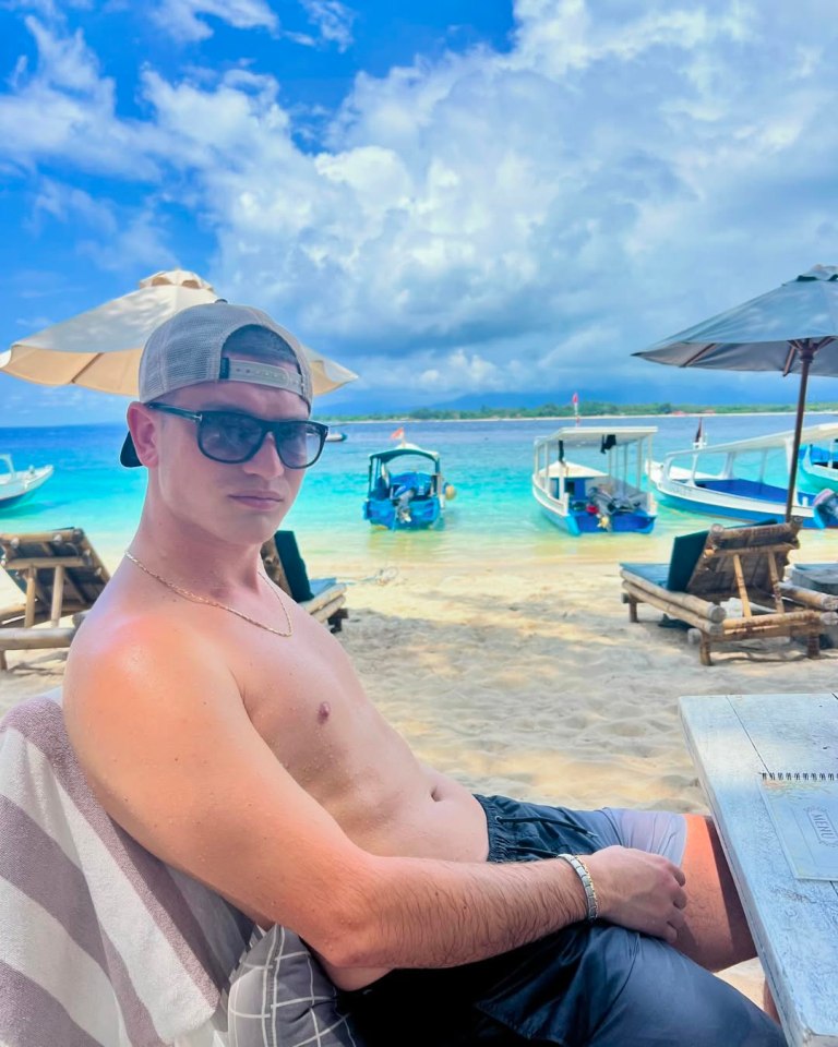 Man relaxing on a beach with boats in the background.