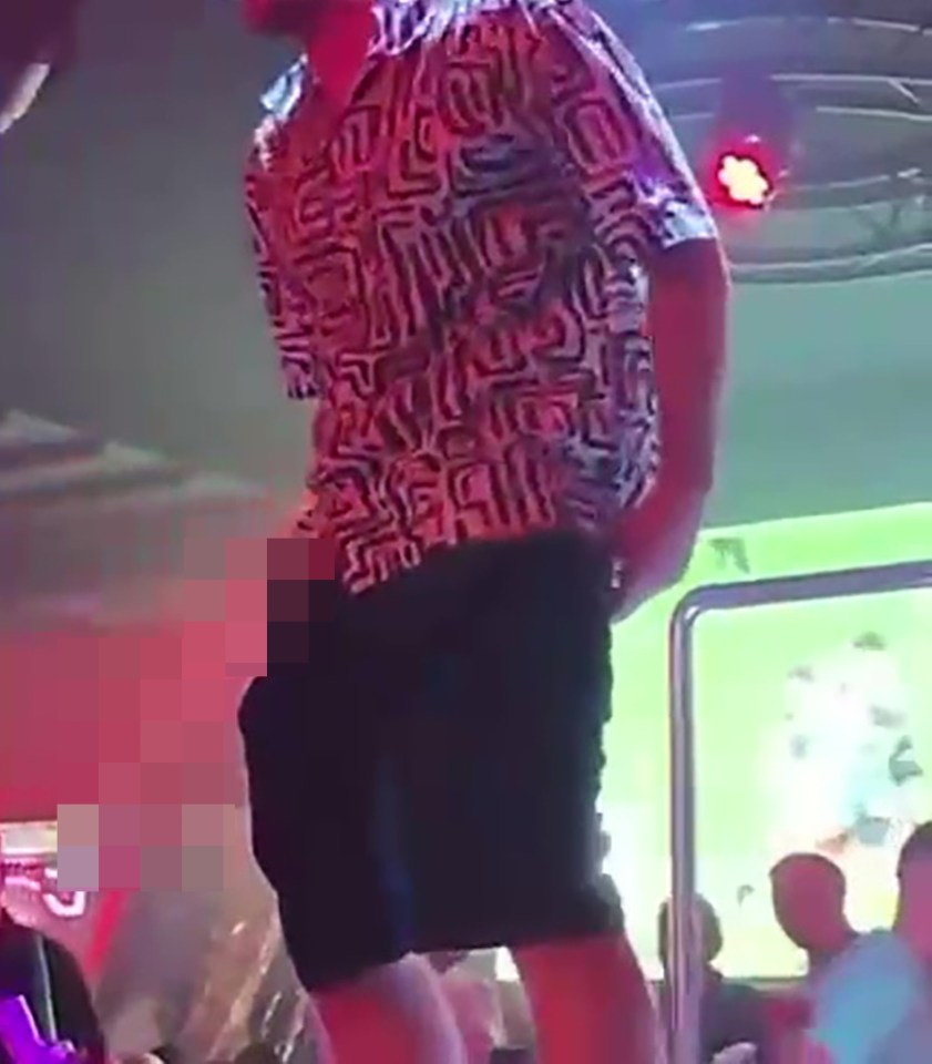 A man urinating on a stage in a crowded bar.