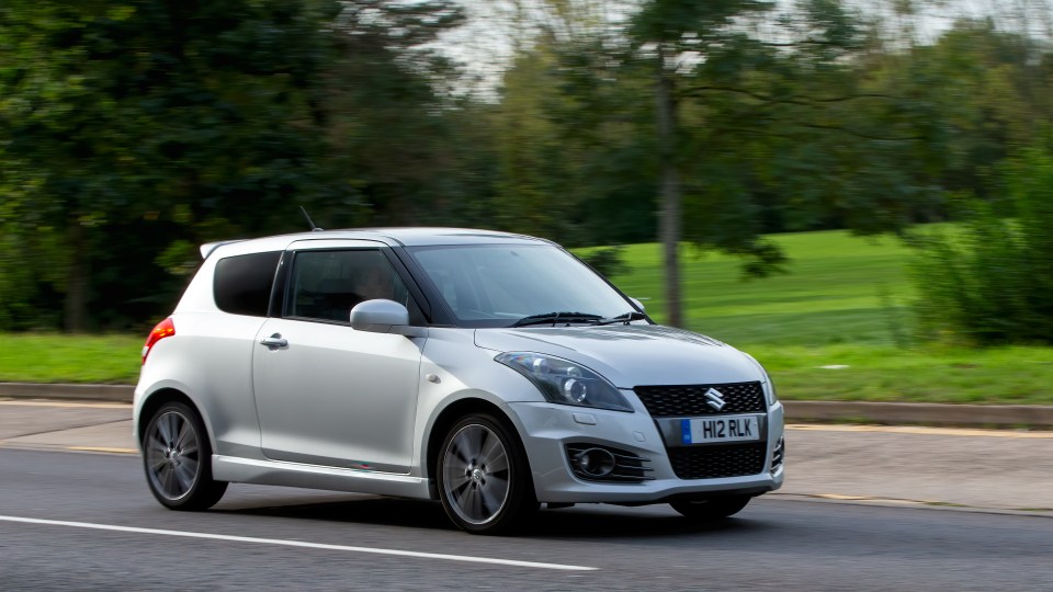 A silver 2012 Suzuki Swift driving down a road.
