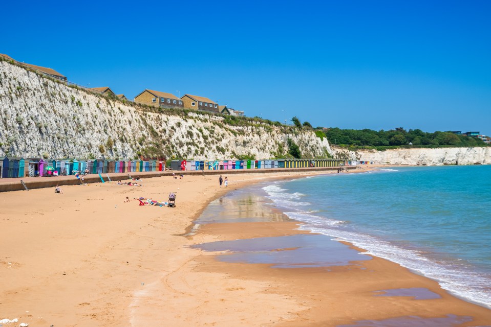 Stone Bay beach in Broadstairs, England, with colorful beach huts and white cliffs.