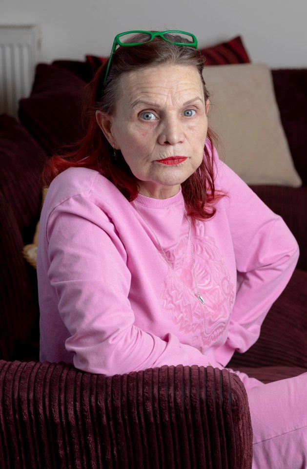 A woman sits on a corduroy couch, wearing a pink sweatshirt.