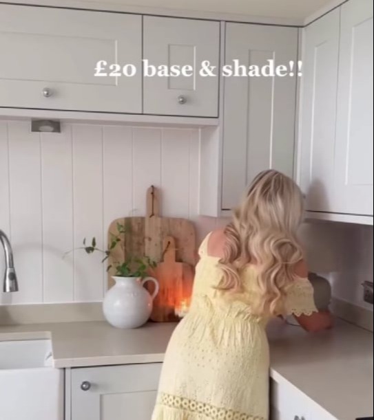 Woman in yellow dress showing off a £20 table lamp.