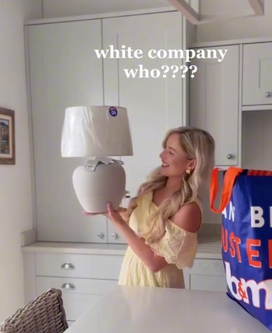 Woman holding up a table lamp, a B&M dupe of a White Company lamp.