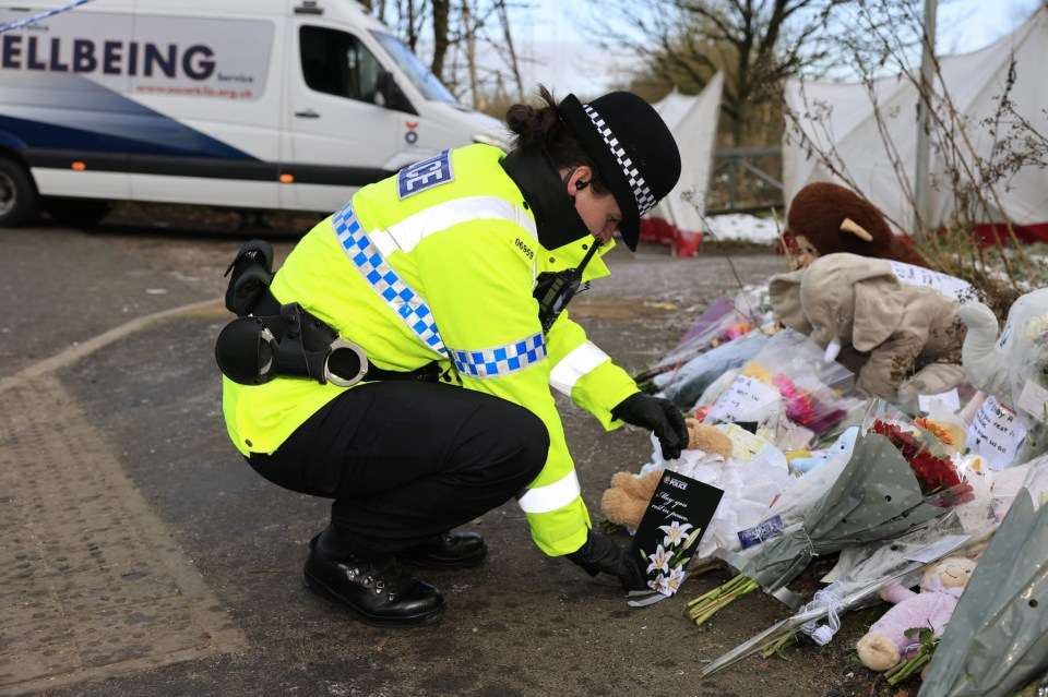 Police officer placing a card among flowers and stuffed animals left as tributes.
