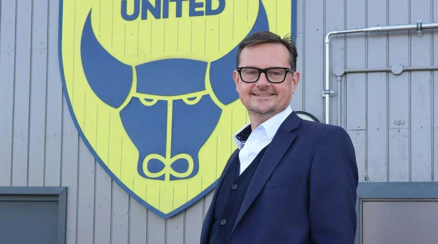 Tim Williams, Oxford United CEO, standing in front of the club logo.
