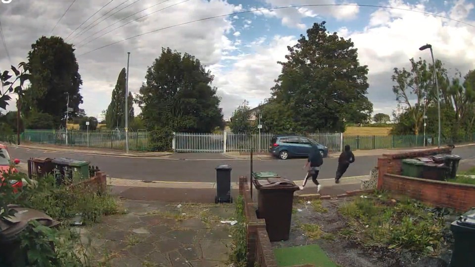 CCTV image showing three people walking down a residential street, near a house with boarded-up windows.