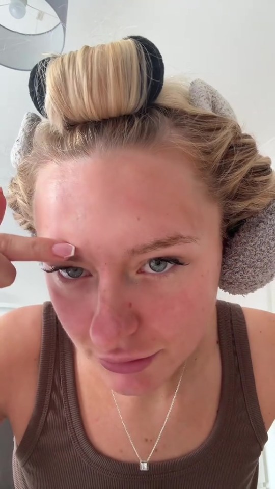 Woman with hair rollers touching her forehead.