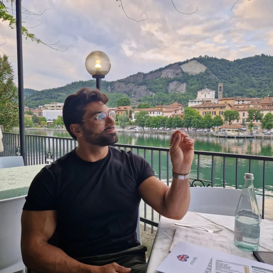 Luke from Married at First Sight sitting at an outdoor restaurant overlooking a lake and town.
