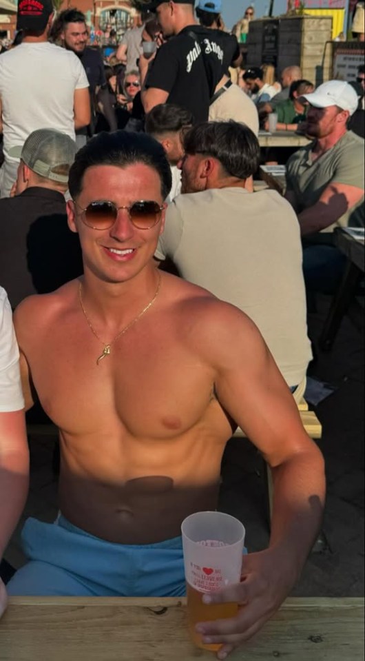 Shirtless man holding a drink at an outdoor event.