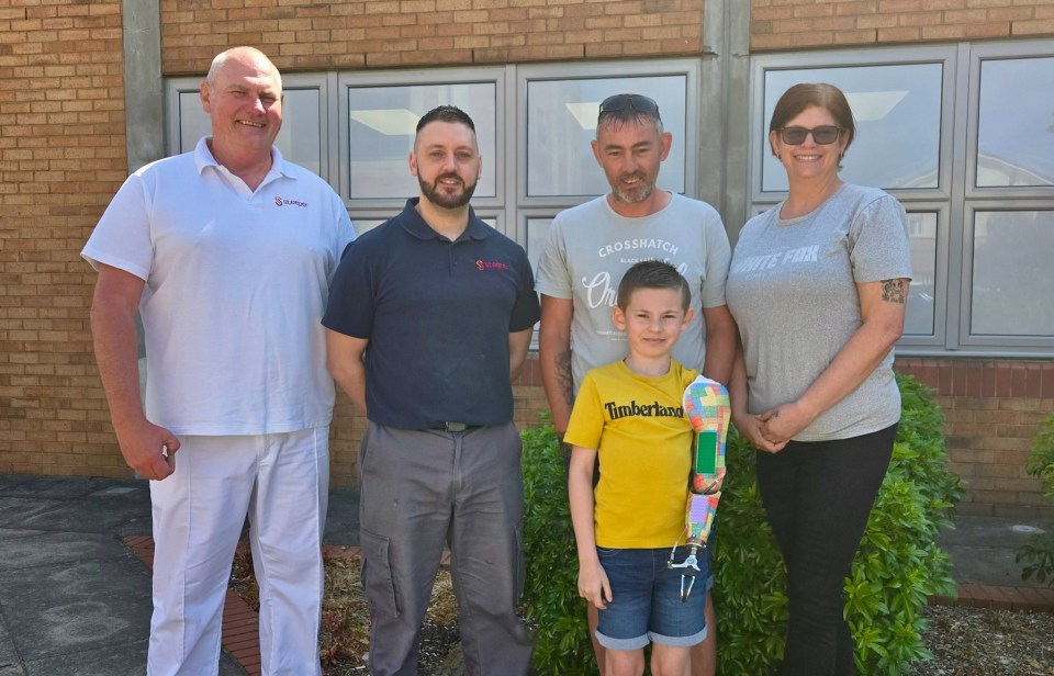 A boy with a Lego prosthetic arm stands with his parents and two adults.