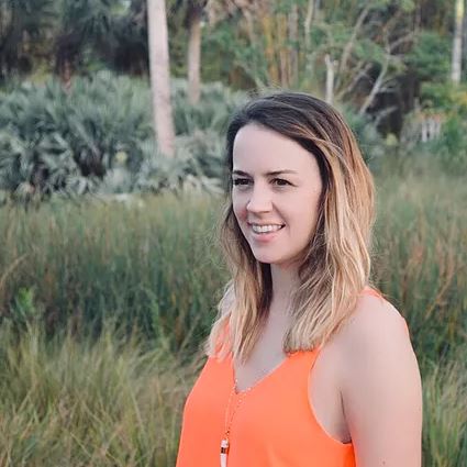 Woman in orange tank top smiling outdoors.