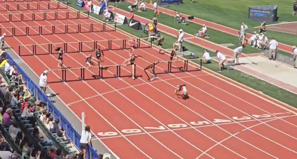 A runner falls during a hurdle race, but maintains her lead.