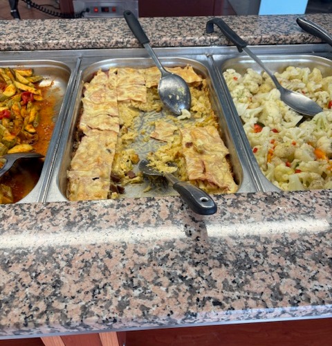 Buffet-style food serving containers with baked casserole, roasted vegetables, and cauliflower.
