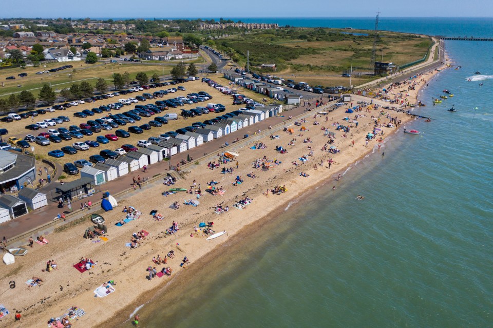 Aerial view of a crowded beach with beach huts and a parking lot.