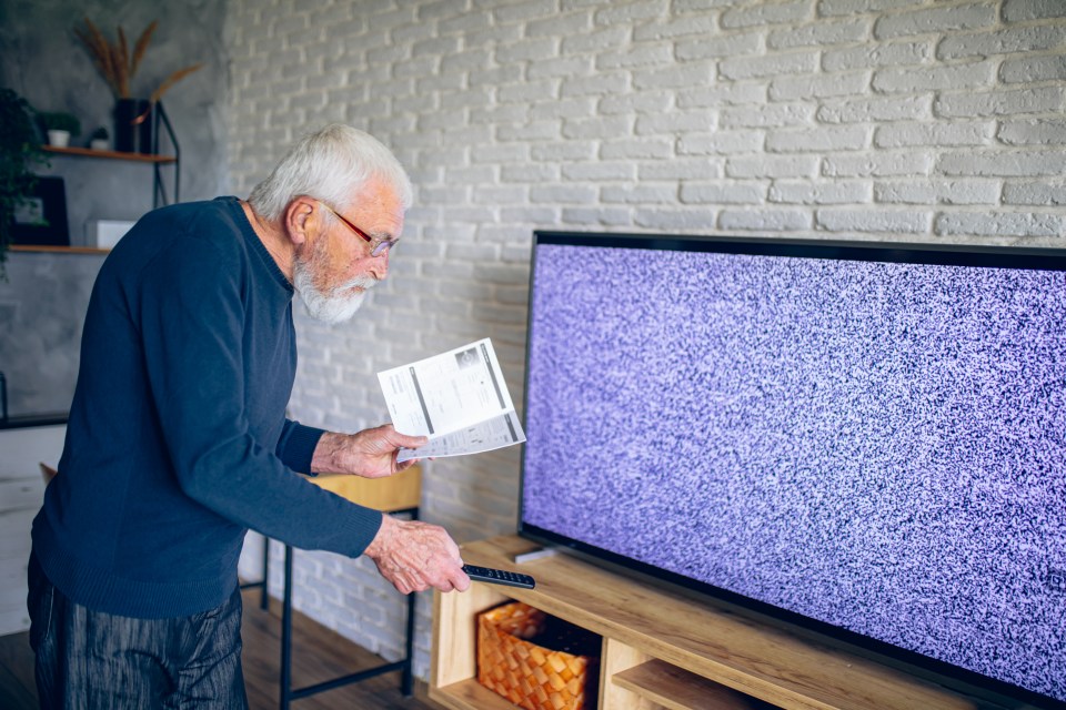 Senior man troubleshooting his television with instructions.