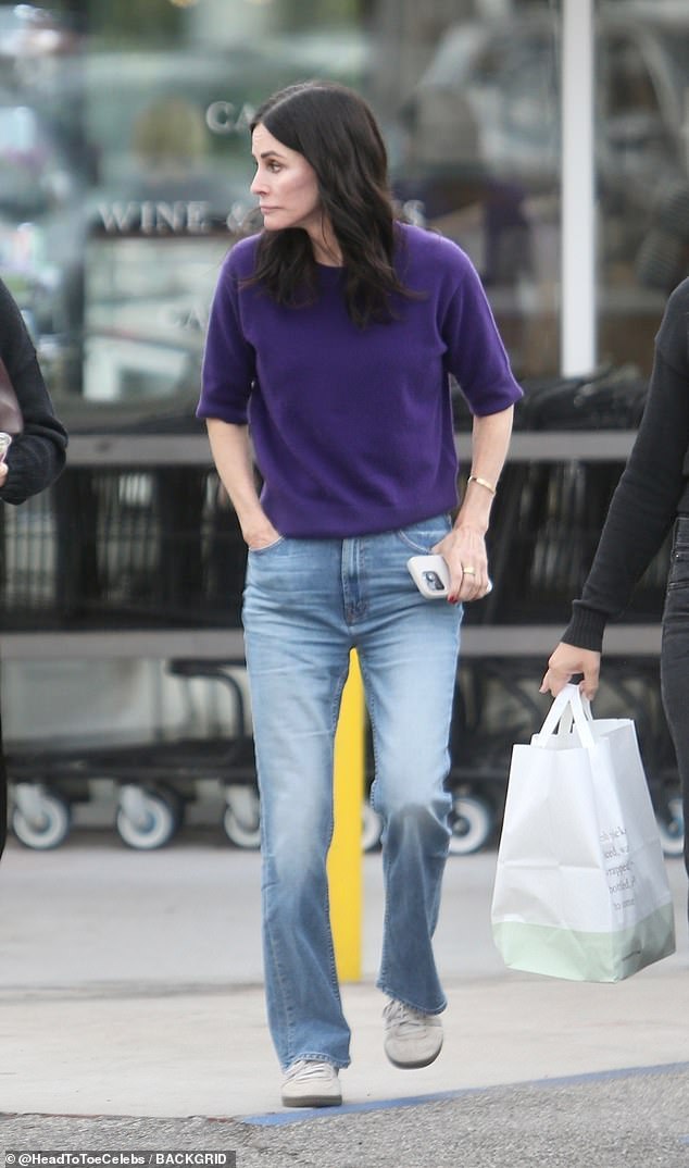 She was comfortably dressed in a crew neck purple sweater, straight-leg, light wash jeans, and gray sneakers