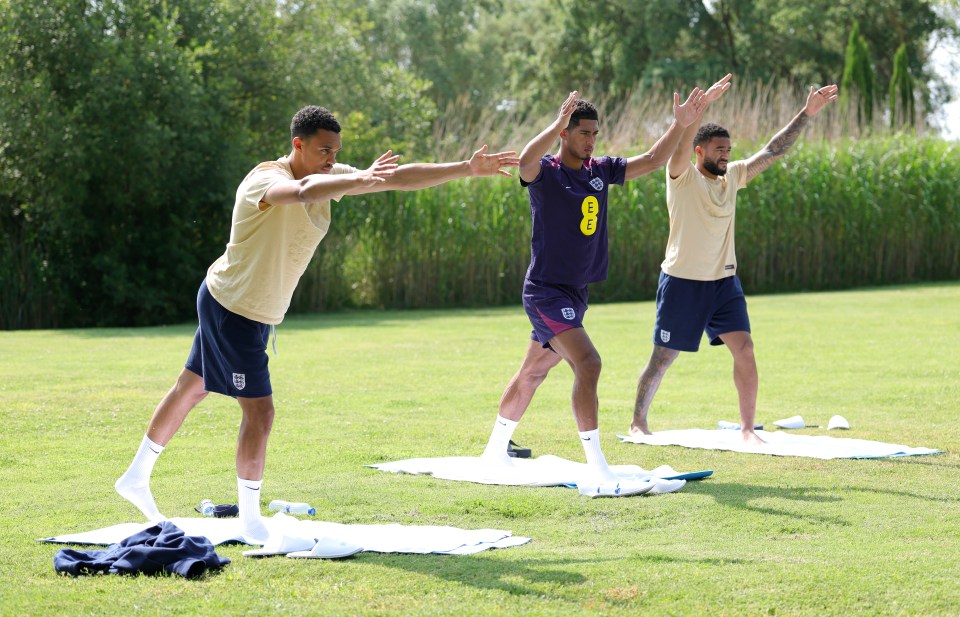 Three England soccer players stretching on mats outdoors.