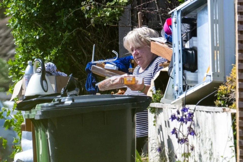 Woman holding food near overflowing bins and discarded items.