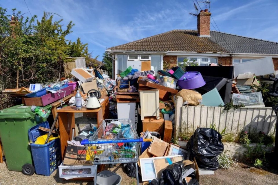 Pile of discarded furniture and household items in front of a house.