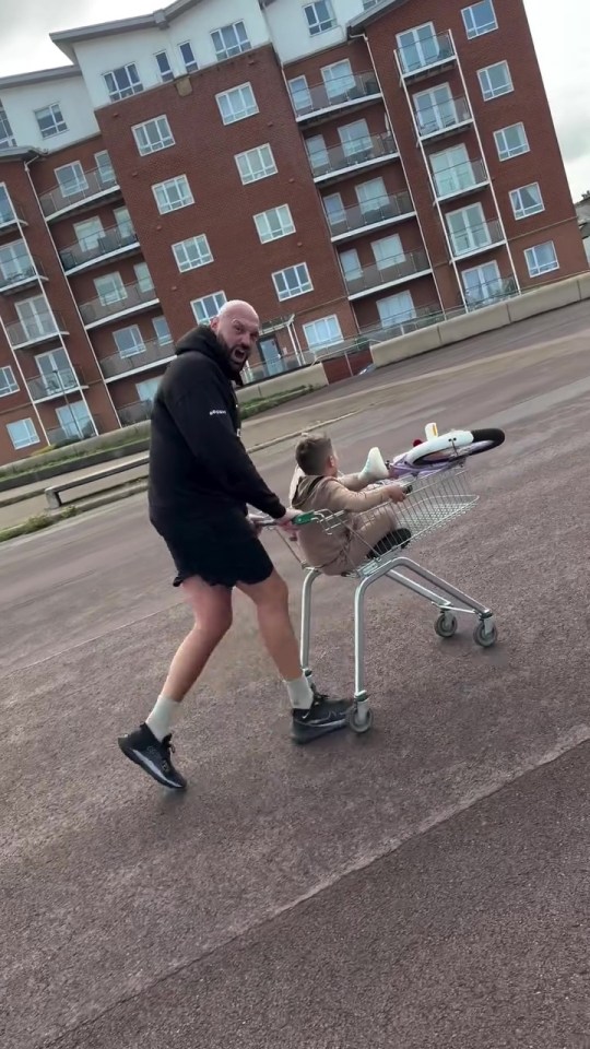 Tyson Fury pushing a shopping cart with a child and bicycle.