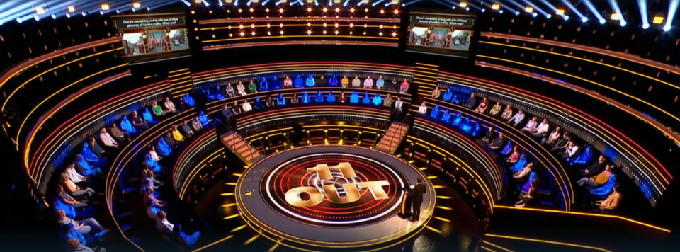Overhead view of the 11 Out game show set with contestants seated in a circular tiered arrangement.
