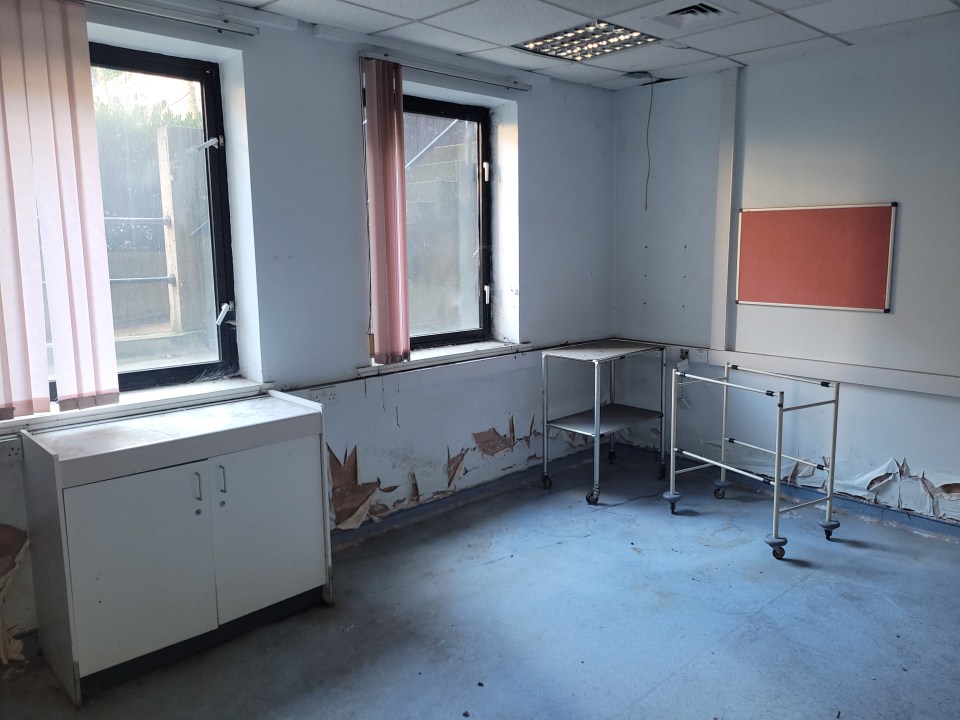 Neglected hospital room with peeling paint and medical carts.