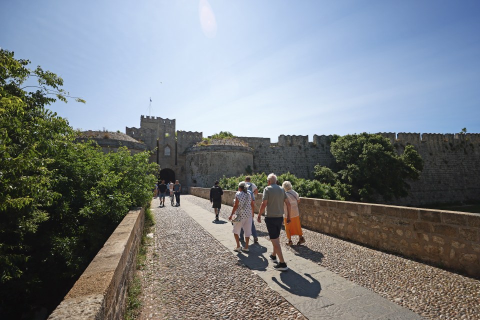 Tourists walking across a stone bridge toward the entrance of a medieval castle.