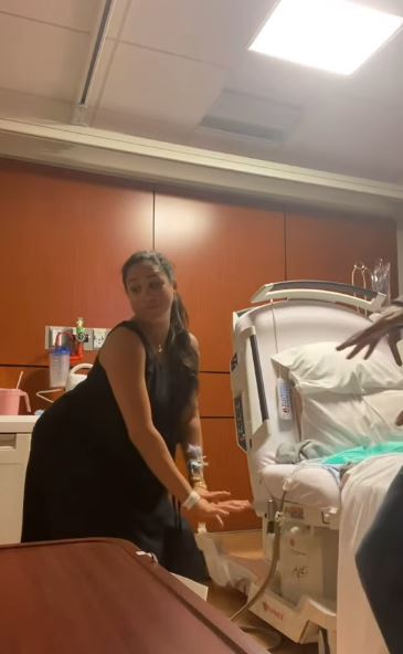 Woman in black dress by hospital bed.