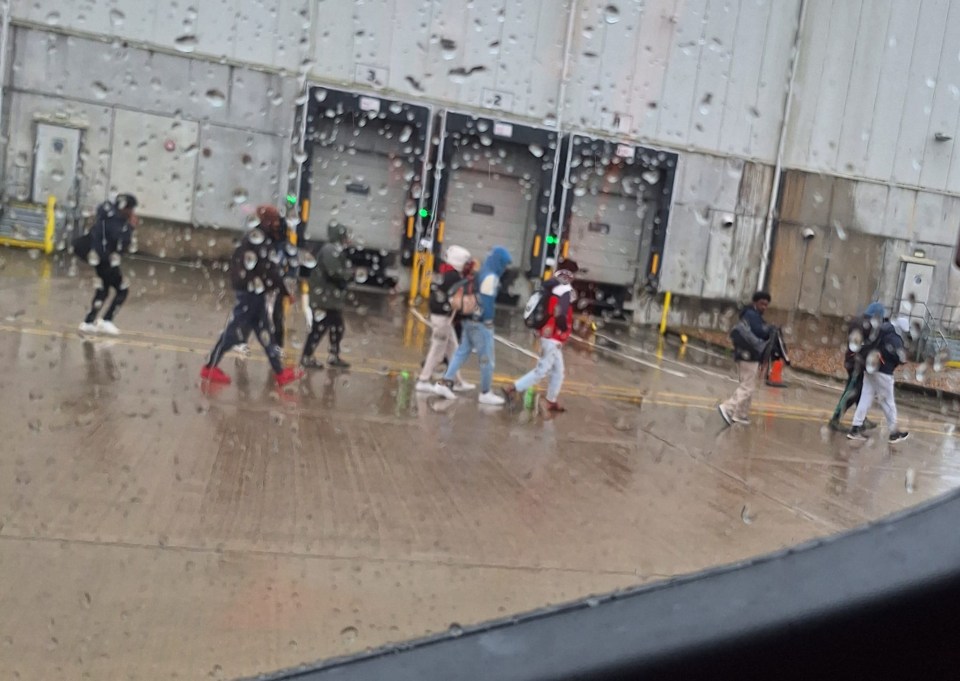 People detained in the rain outside a warehouse.