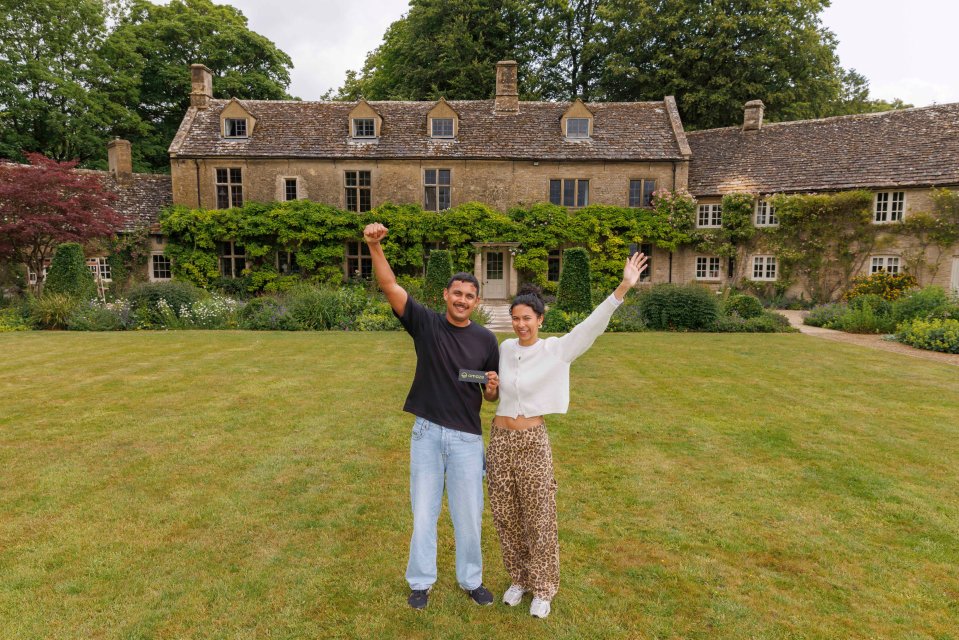 A man and woman celebrating in front of a large Cotswolds home they won in an Omaze contest.