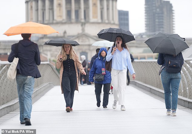 People with umbrellas walking along the Millennium Bridge in London in the rain yesterday