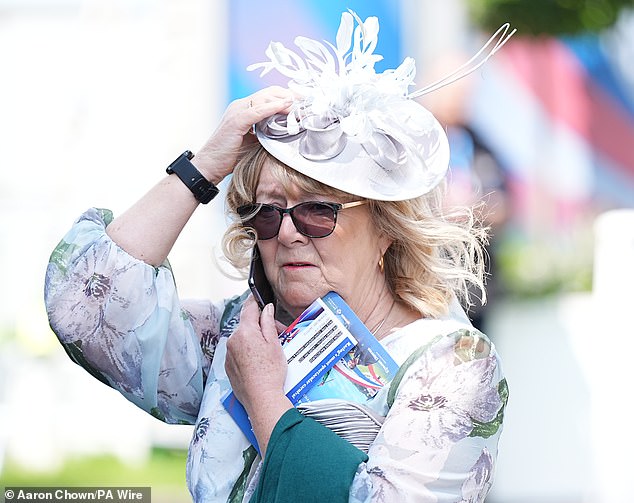 Though the rain appeared to have eased off, racegoers still held onto their hats amid the wind