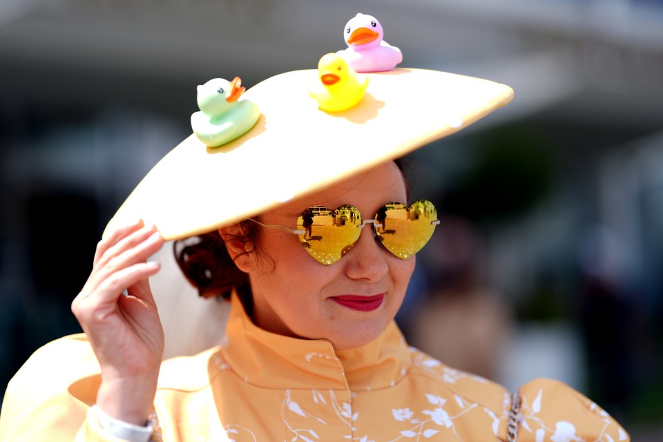 Woman wearing a large hat decorated with rubber ducks and heart-shaped sunglasses.