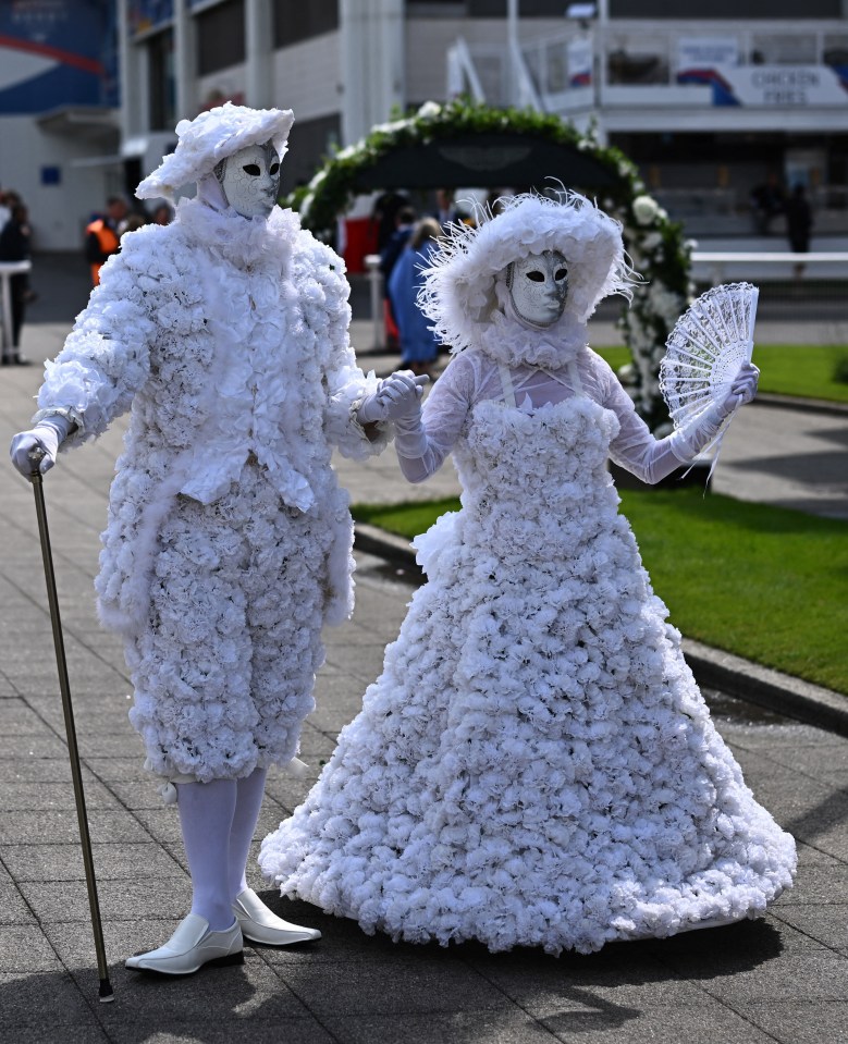 Woman photographing performers in white floral costumes at a racecourse.