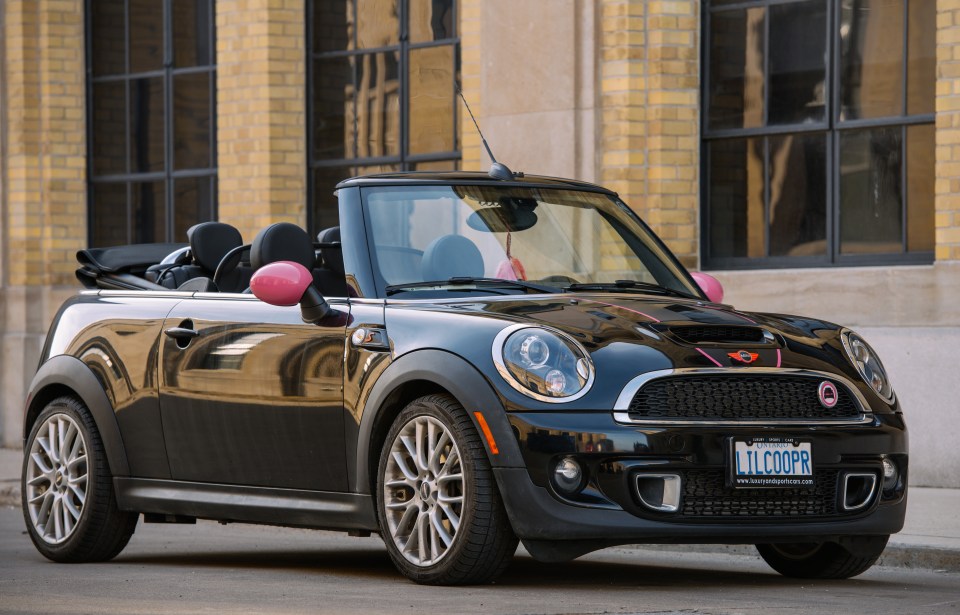 Black Mini Cooper convertible parked in front of a brick building.