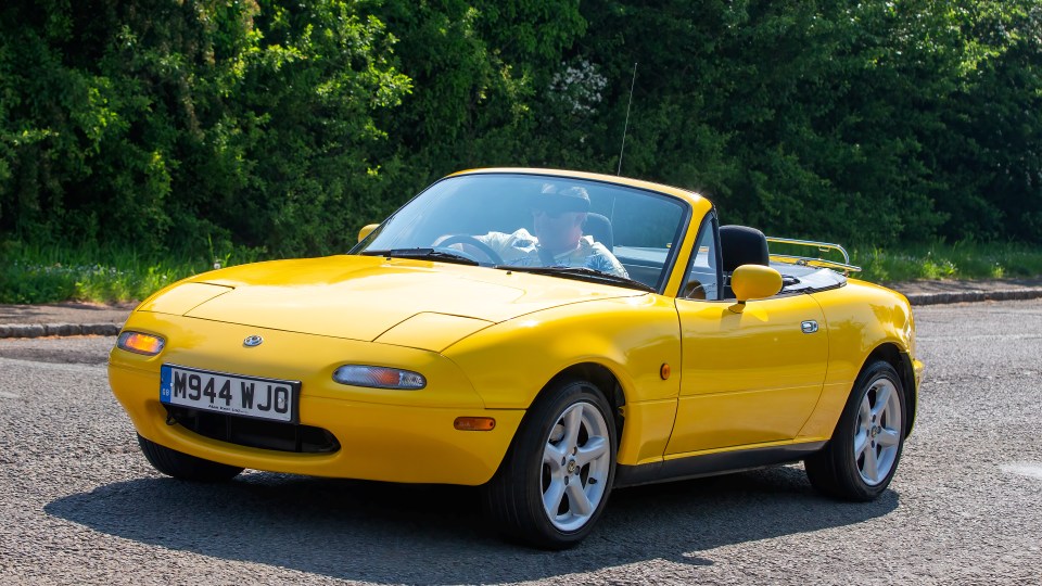 Yellow Mazda MX-5 Miata convertible driving on a road.
