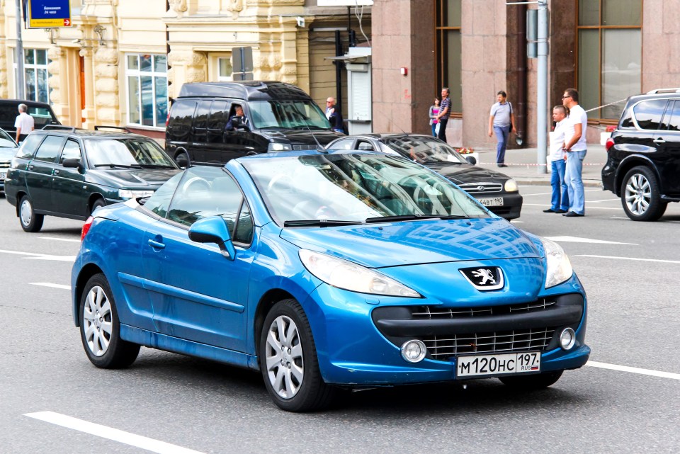 Blue Peugeot 207 CC convertible driving on a city street.