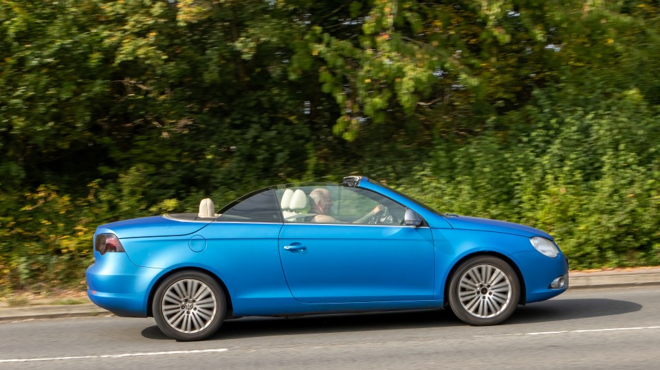 Blue convertible driving down a road.