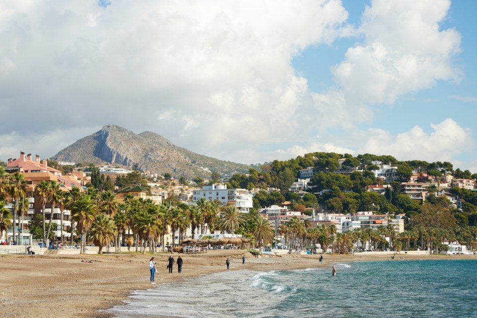 Beach in Malaga, Spain, with buildings and a mountain in the background.