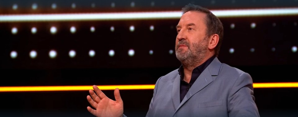 A man in a suit gestures during a game show.